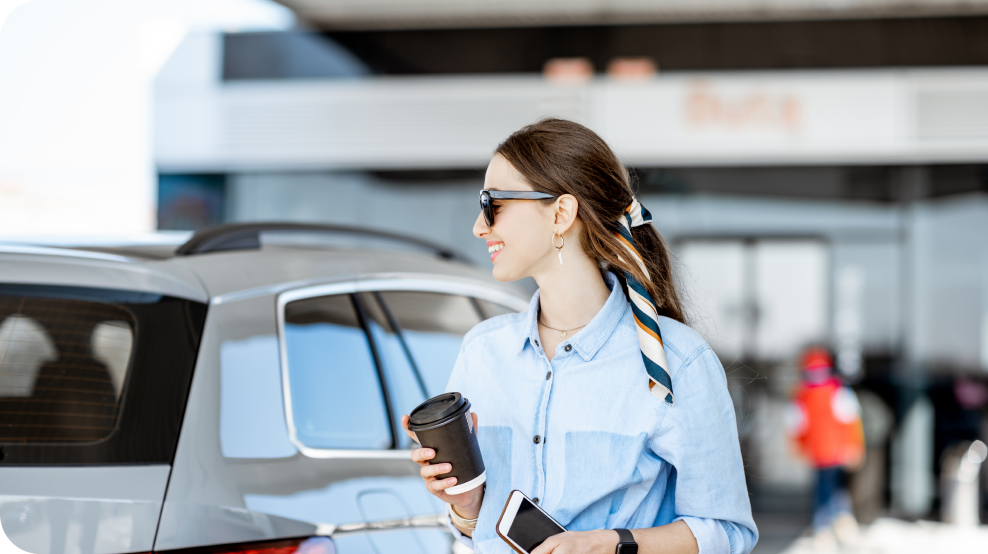 A woman holding a coffee at the gas station.