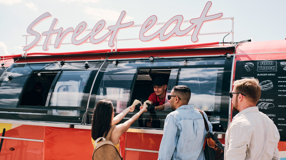 A young female buyer is taking a hotdog from the food truck.