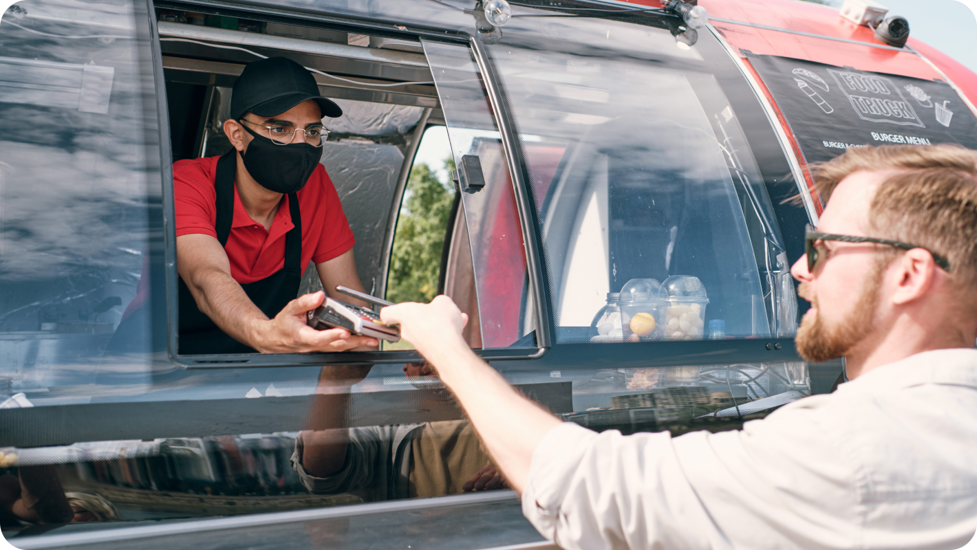 A young man holding a smartphone over the payment terminal at the checkout counter of the food truck.