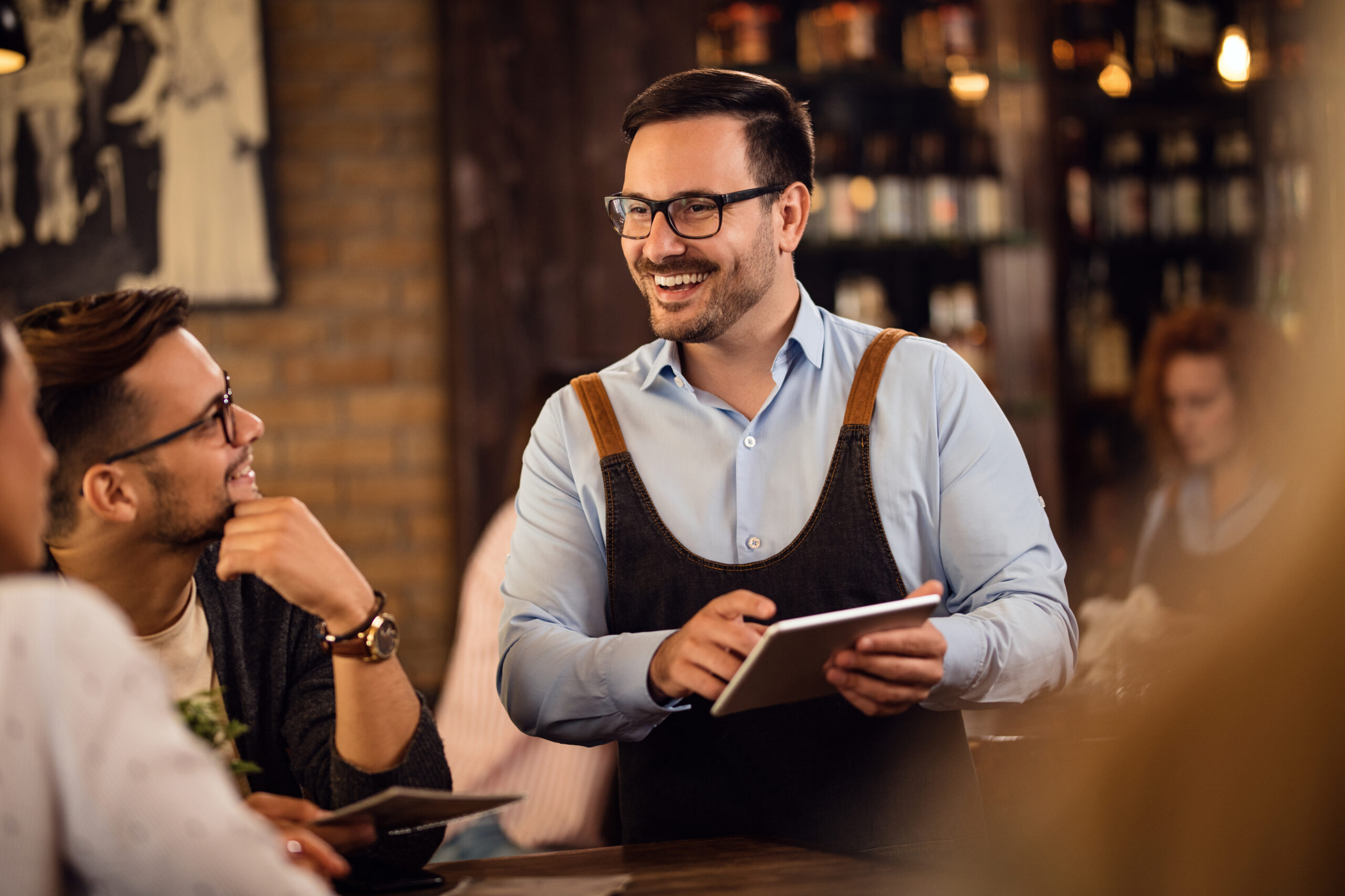 An employee standing near the guest table is holding a tablet.