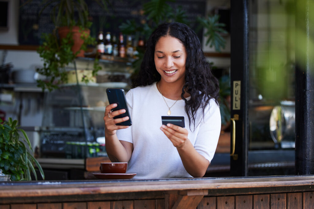 A young woman is making payment on her phone while sitting in a cafe.