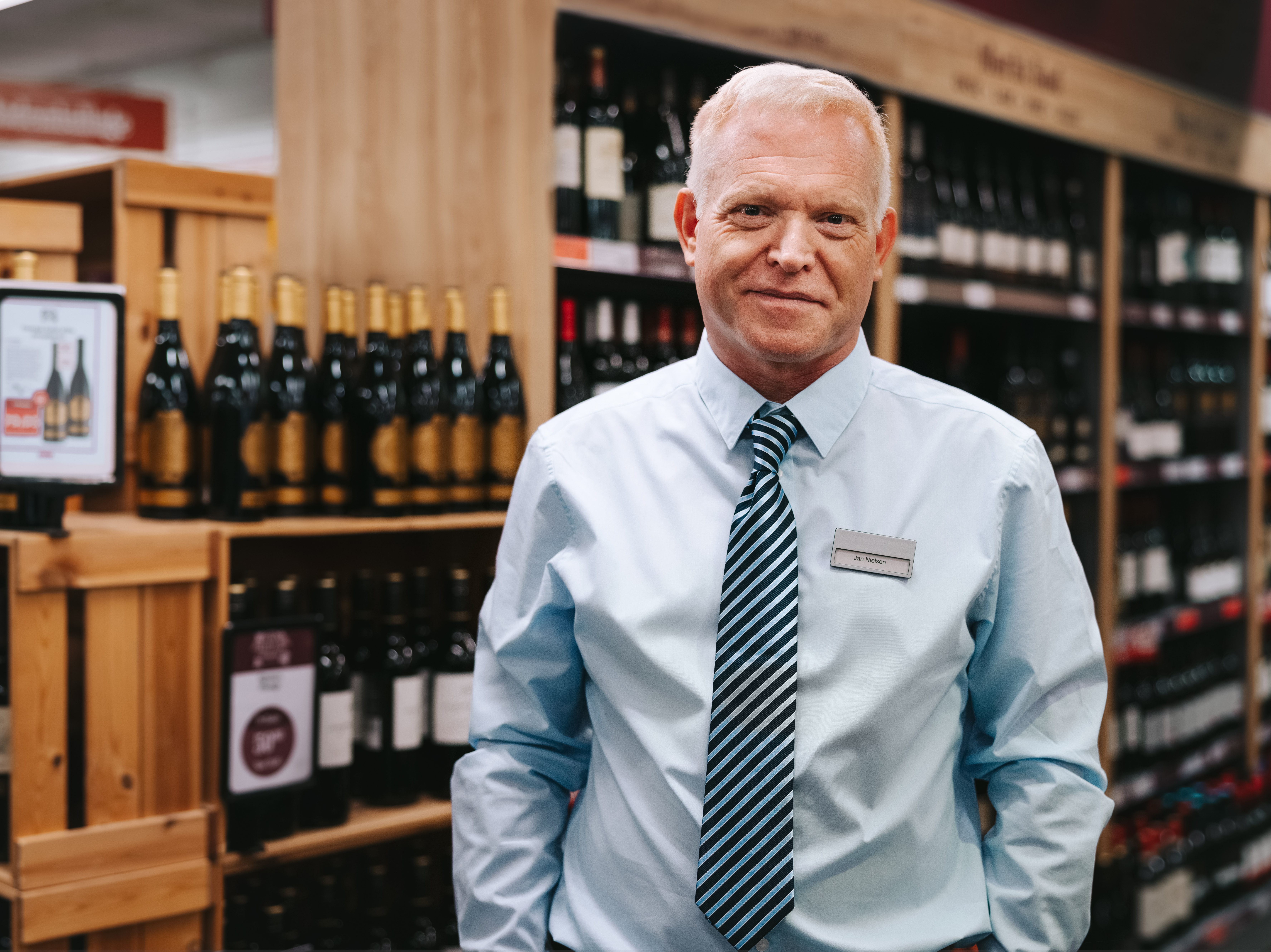 A liquor store employee is standing in the liquor section.